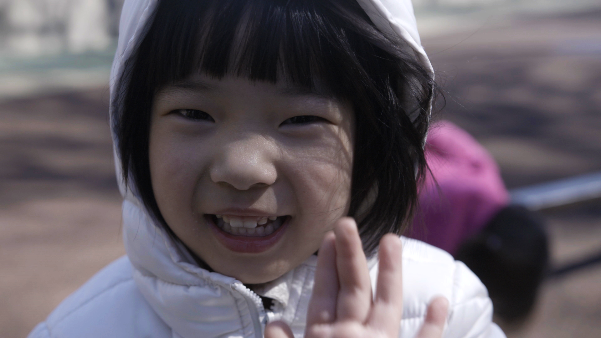 A smiling child in a white hooded jacket.