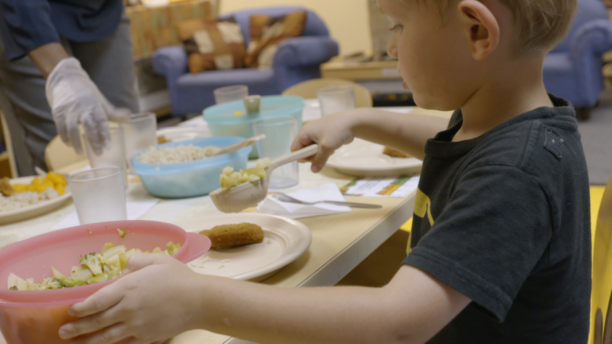 A child scooping vegetables onto a plate at a table set for a meal.