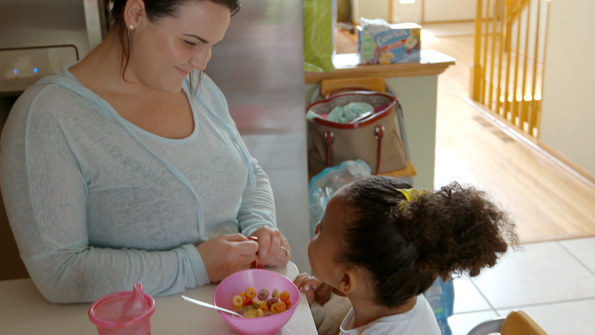 A woman and a young girl at a kitchen counter with a bowl of cereal.