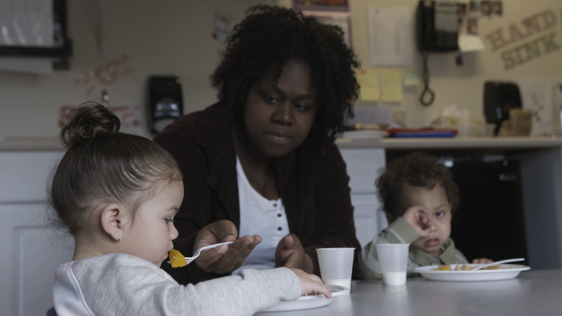 An adult interacting with two children at a table with plates and cups.