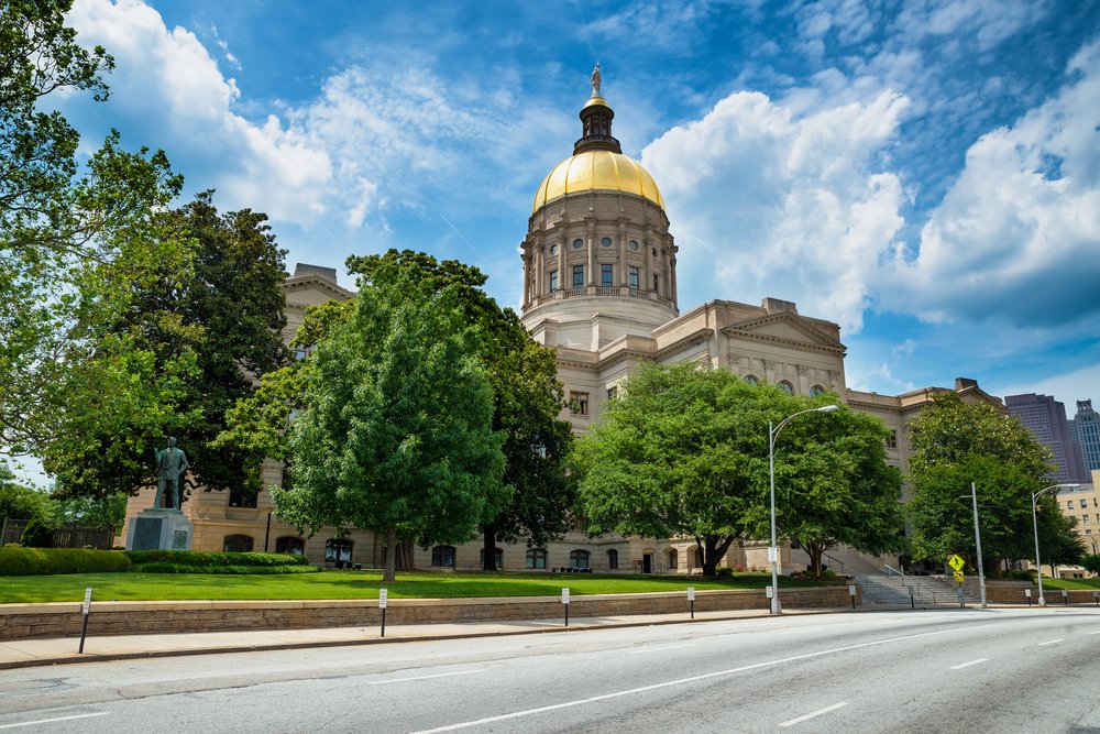 Georgia State Capitol with a gold dome surrounded by trees and a blue sky.