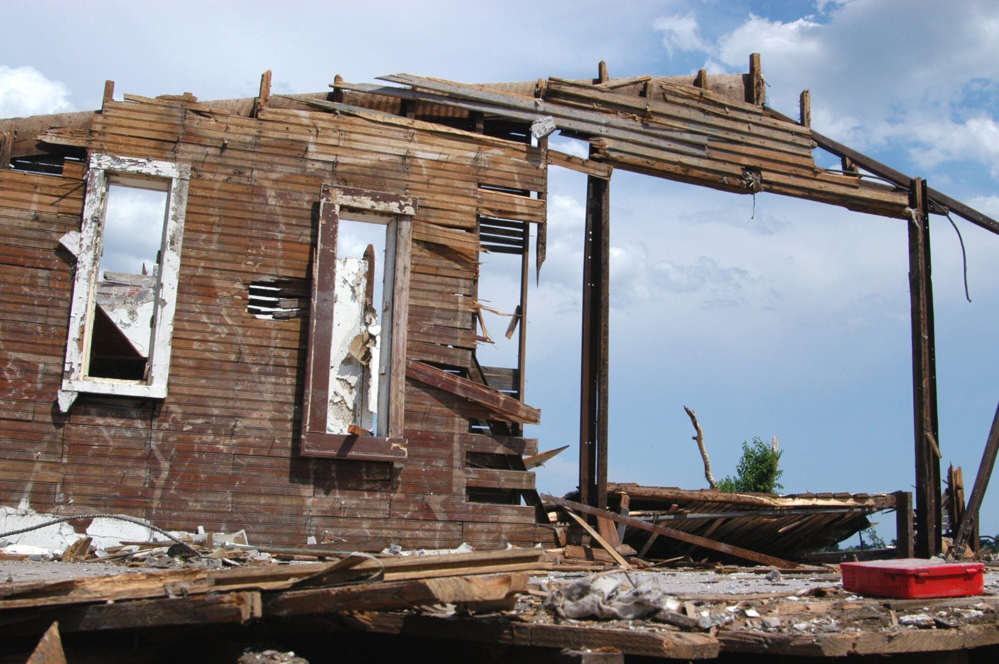 A partially collapsed wooden building with exposed frames and debris, including a red toolbox.