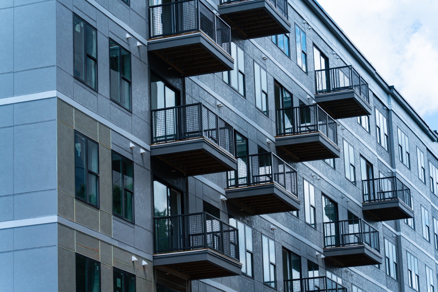 A modern apartment building with multiple balconies and large windows, featuring a metallic gray exterior.