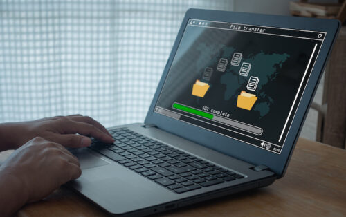 Hands on a laptop that shows files transferring from one folder to another.