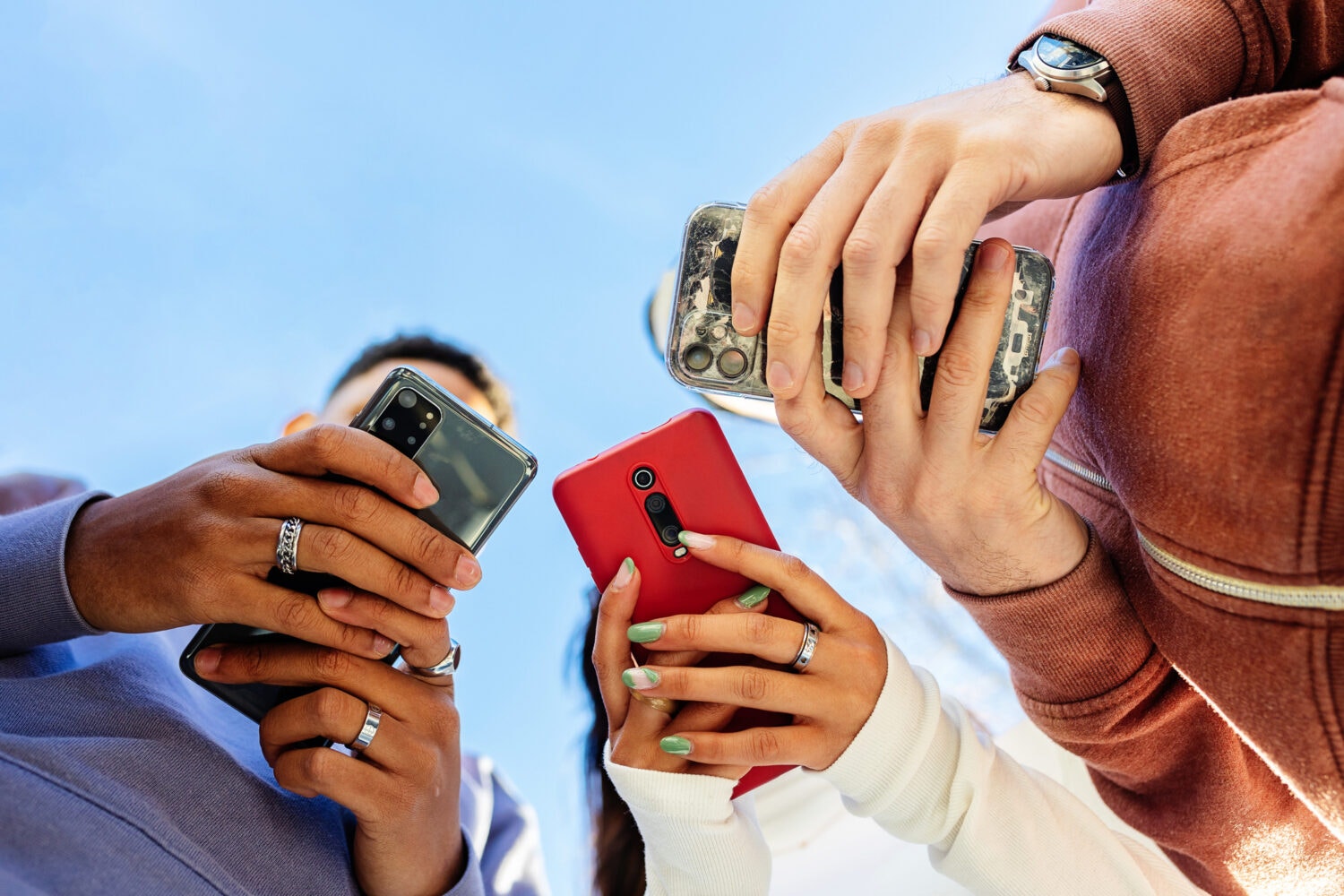 An upward shot of three people holding cell phones. Their phones obscure their faces.