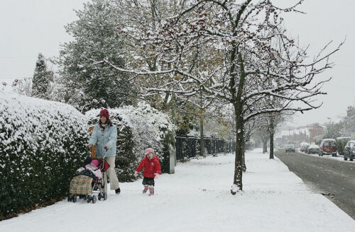 Families walks in a neighborhood and enjoys the winter weather and snow fall.