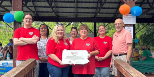 Seven people under a pavilion, four in red shirts with a plaque.