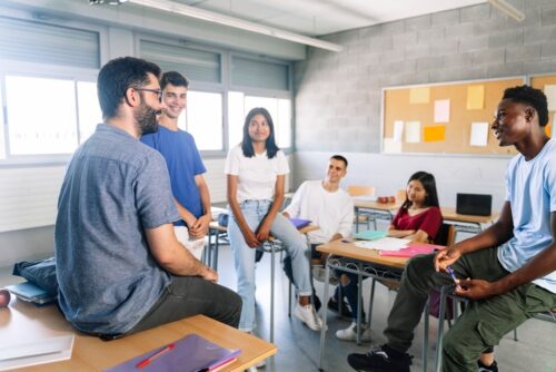 group of teenagers crowds around adult in a classroom