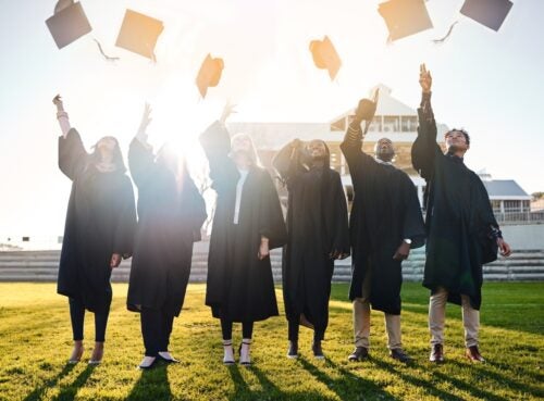 six college graduates toss their graduation caps in the air with the sun shining behind them