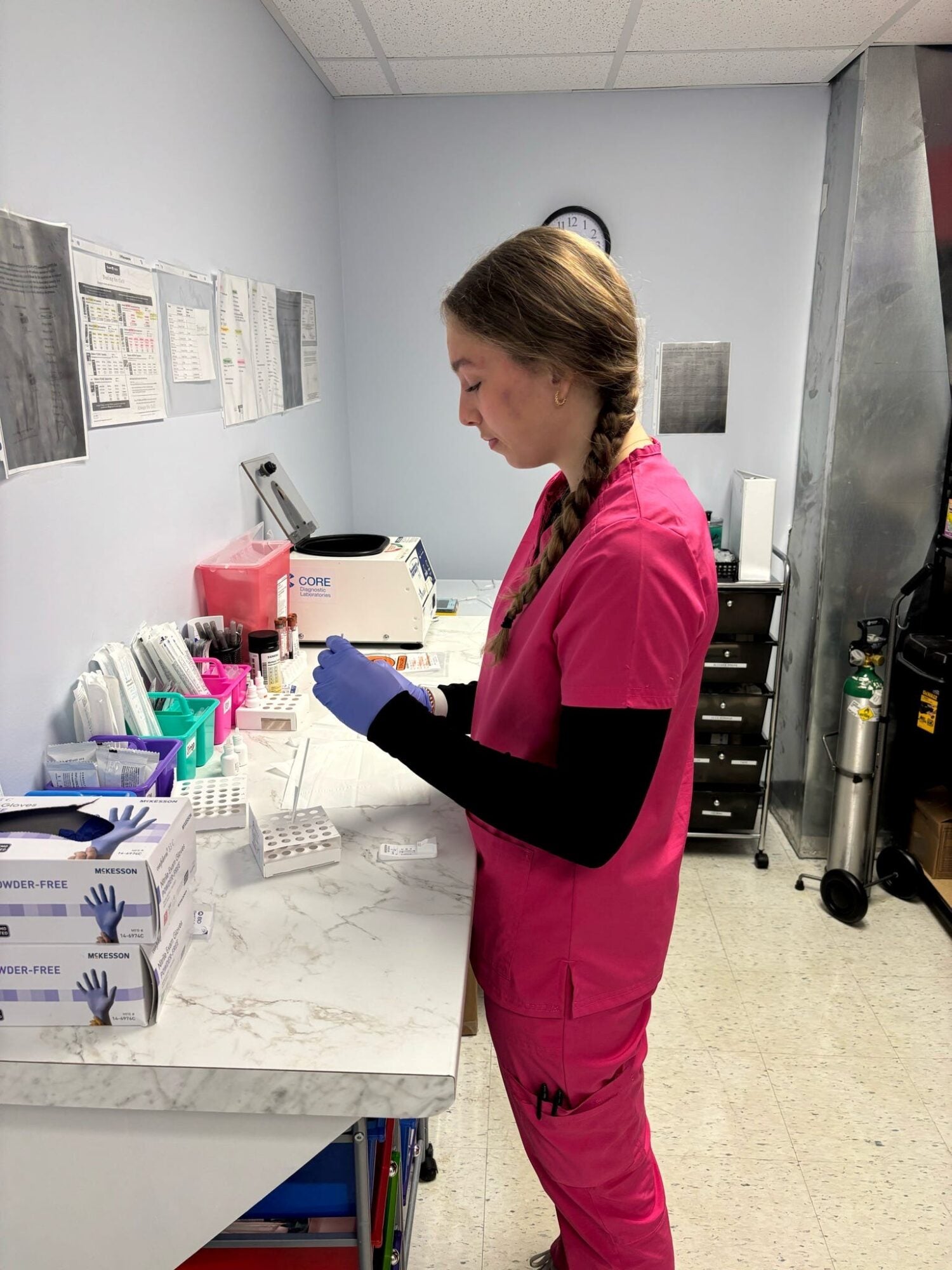 a certified nursing assistant wears pink scrubs in an office setting.