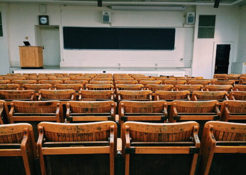 Rows of brown chairs facing to a college-style classroom lecture hall, which is empty.