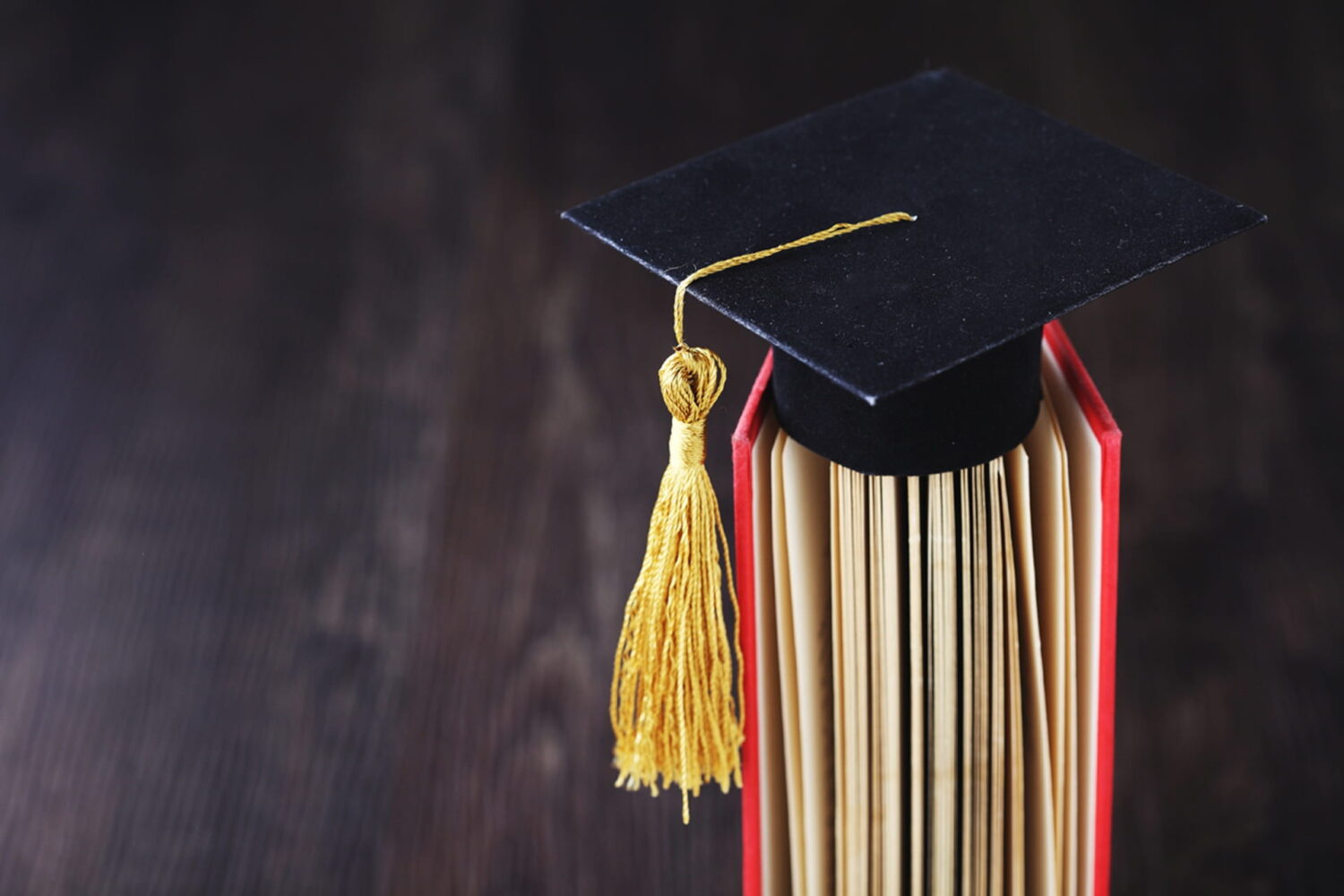 A small graduation hat, sitting on top of a book, with its tassel moved to the side