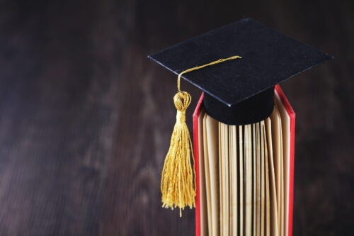 A small graduation hat, sitting on top of a book, with its tassel moved to the side