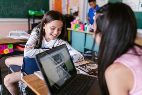 Two students working at a desk are pictured from above their heads.