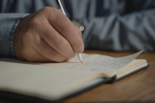 A close up of a hand holding a pen writing in a notebook.