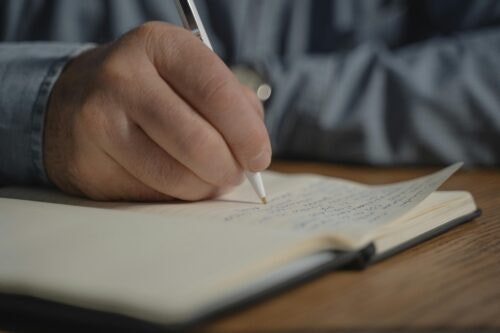 A close up of a hand holding a pen writing in a notebook.