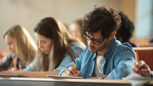 three students taking an exam with pencil and paper