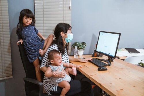 Mom wearing mask carrying her baby while working from home office
