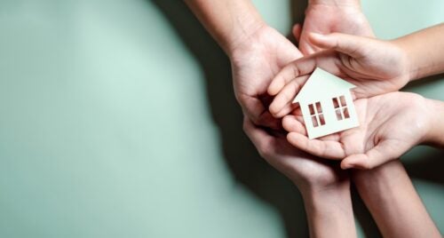 Hands Holding Wooden House on blue background