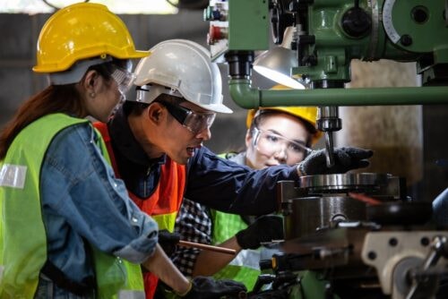 Industrial maintenance mechanic repairs manufacturing equipment with two co-workers