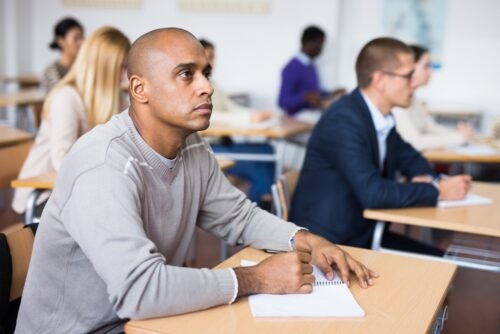Hispanic man listens intently to teacher and takes notes in an adult education class