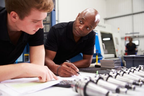 Black male engineer and young white male apprentice work together to plan a Computer Numerical Control machinery project