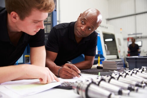 Black male engineer and young white male apprentice work together to plan a Computer Numerical Control machinery project