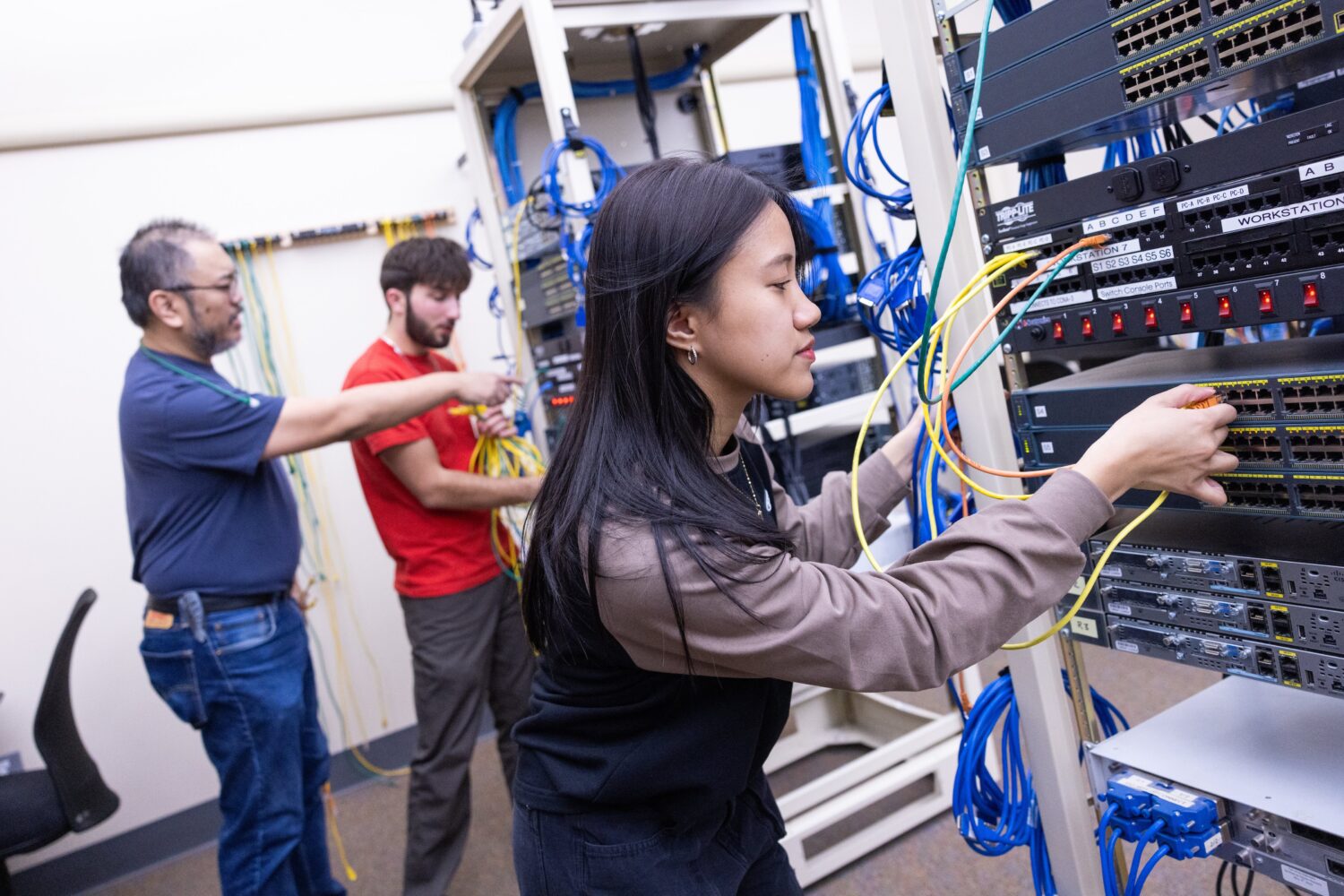 Asian female student connecting machines as a male instructor works with a student in an IT lab on a college campus.