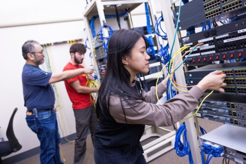 Asian female student connecting machines as a male instructor works with a student in an IT lab on a college campus.