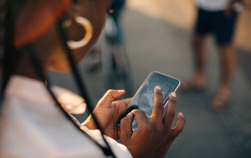 Over-the-shoulder view of woman standing outside while tapping content on her phone.