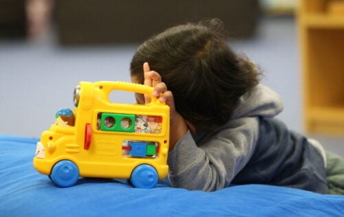 A young child plays with a yellow toy school bus