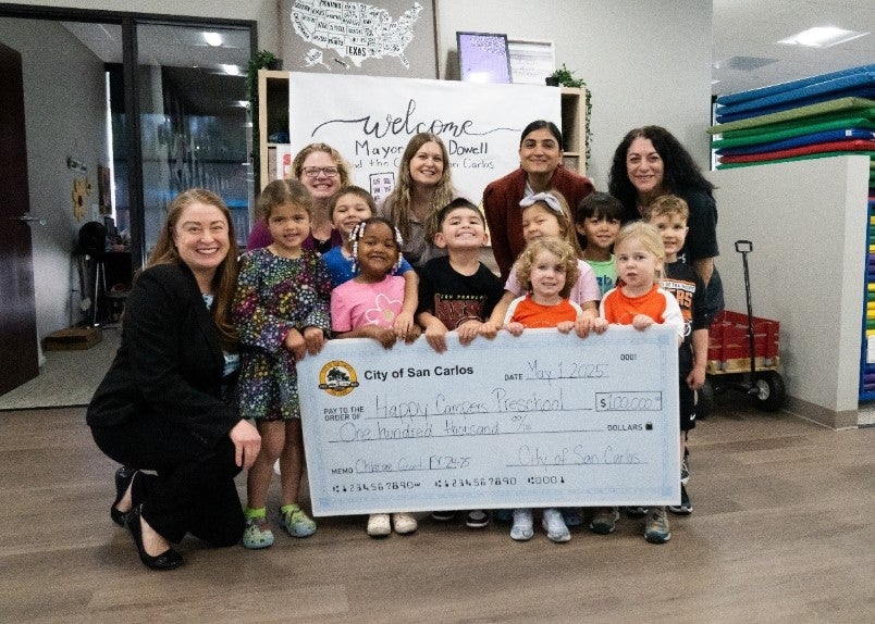 Young children and adults standing behind a large, decorative check