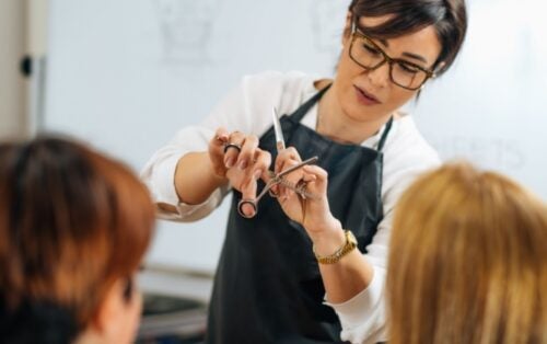 A cosmetology teacher trains two students how to cut hair.