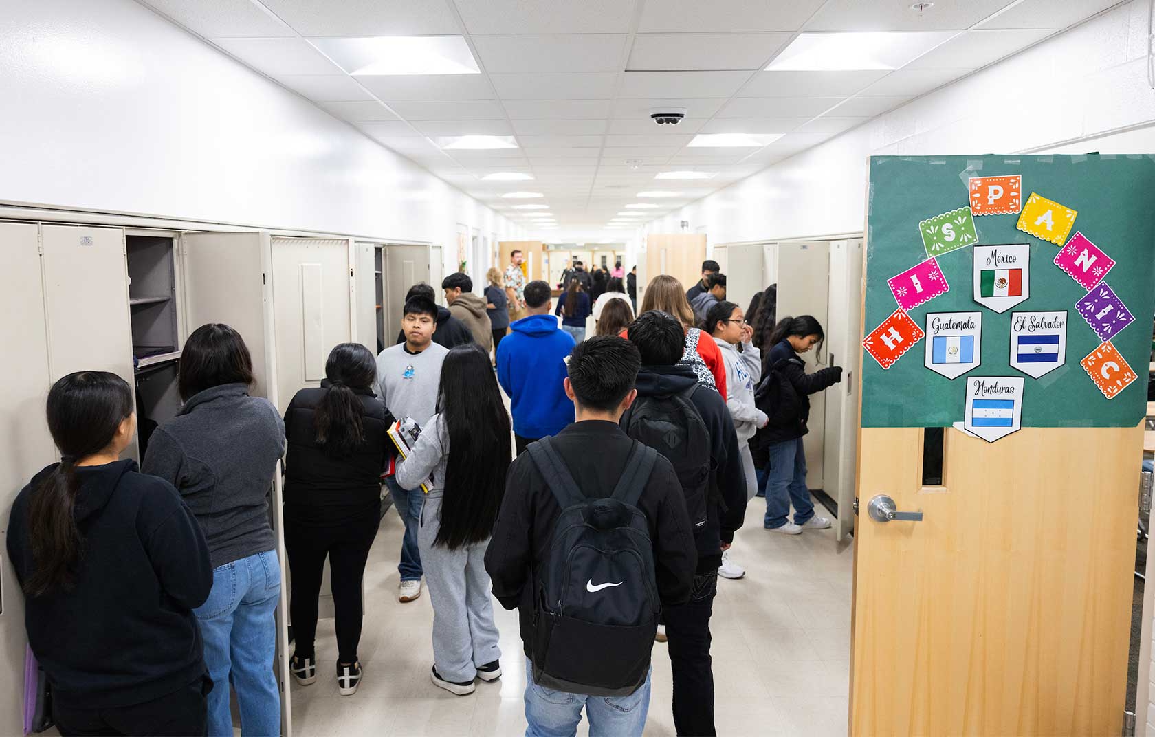 Students gather in a busy school hallway with lockers, a poster displaying 