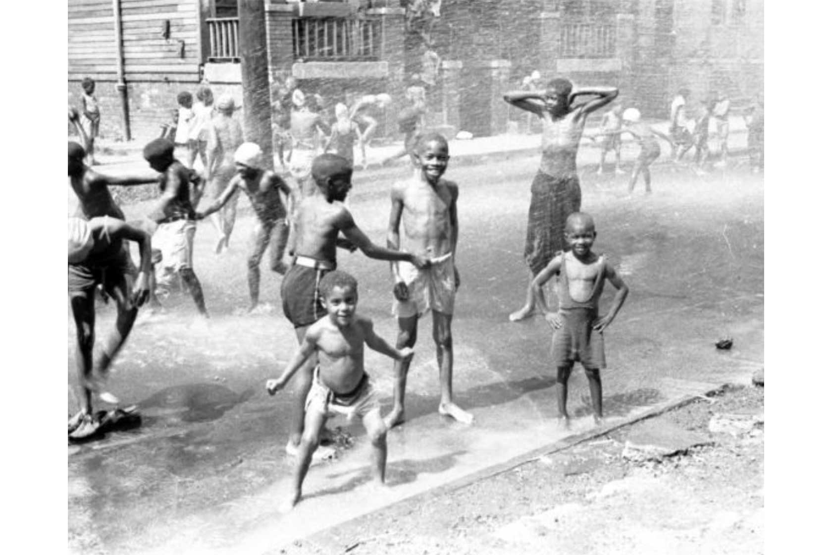 Children playing and splashing in shallow water on a sunny day in an urban setting.