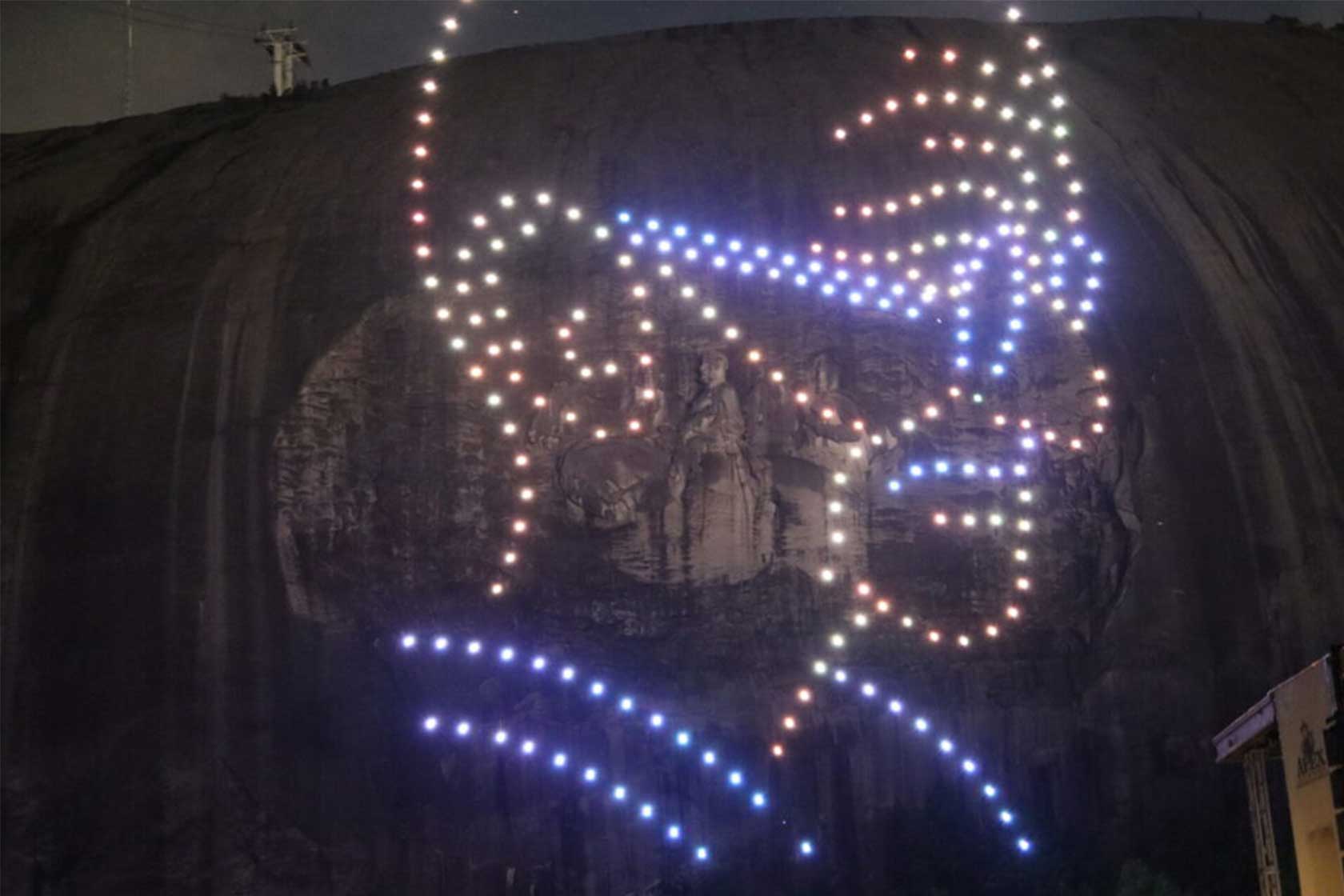 Illuminated rock formation at night, featuring a colorful abstract light display and a carved sculpture of a seated figure.