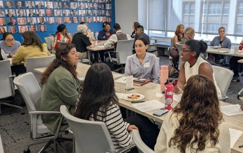 People engaged in discussion around tables in a conference room with portrait-covered walls.