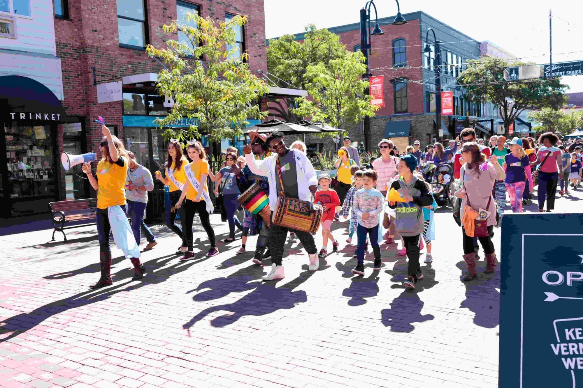 A diverse group of people marching in a vibrant street parade, led by a person with a megaphone and another playing a drum.
