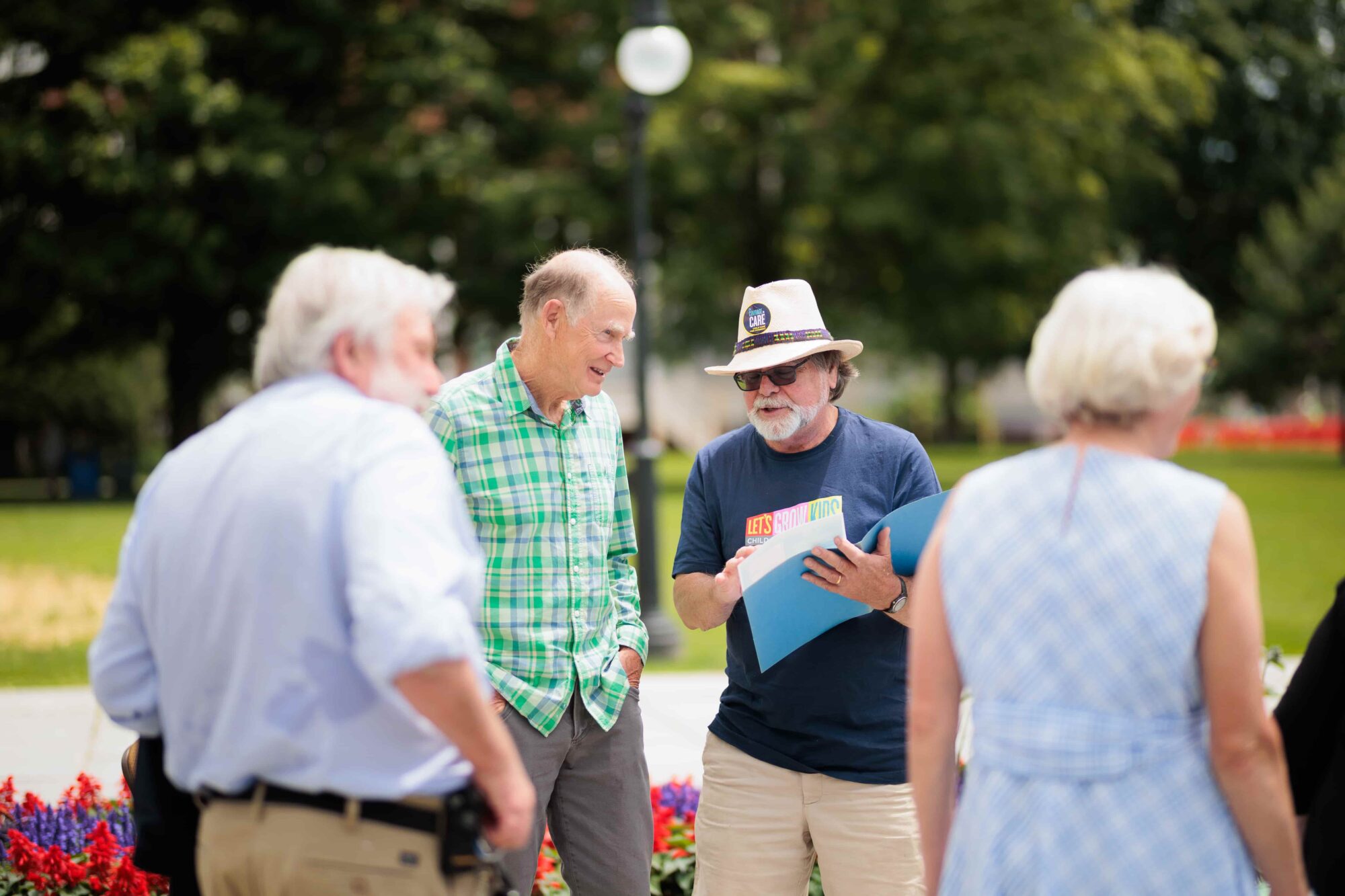 A group of people in conversation outdoors in a park setting.