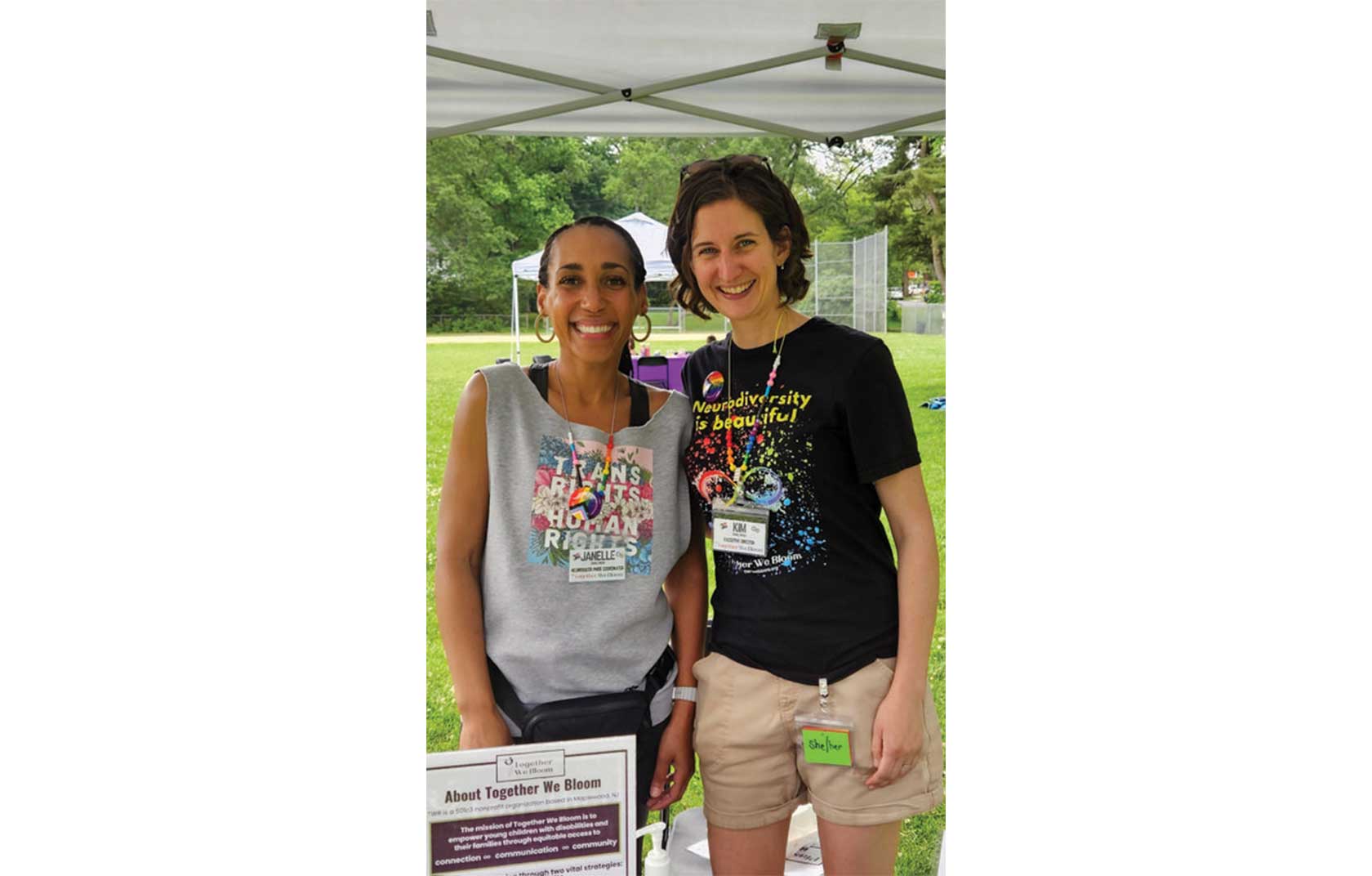 Two smiling women stand together outdoors, one in a gray shirt with 
