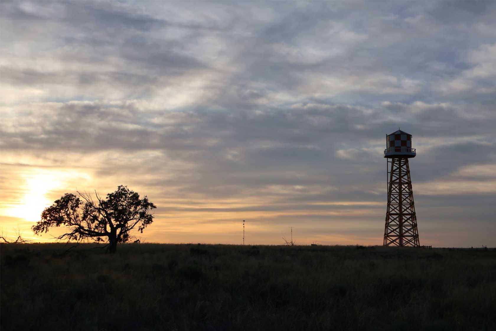 A silhouette of a large tree next to a tall watchtower against a colorful dusk sky, with grass in the foreground.