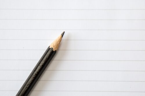 Half of a brown pencil is visible on top of blank lined paper.