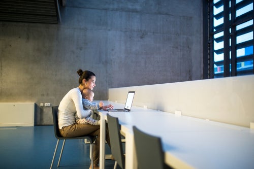 Woman sits with child in her lap and works on laptop