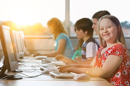 Student with down syndrome smiling at camera in front of computer
