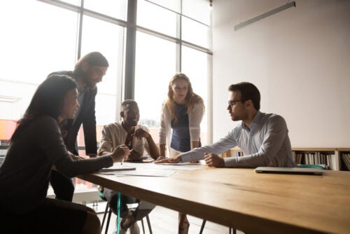 Five employees sit around a table and have a discussion.