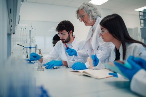 A group of two diverse students sit at a lab table with a professor guiding them.