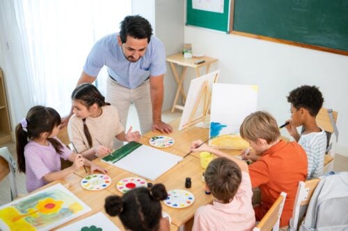 Male teacher helps six students sitting around a table