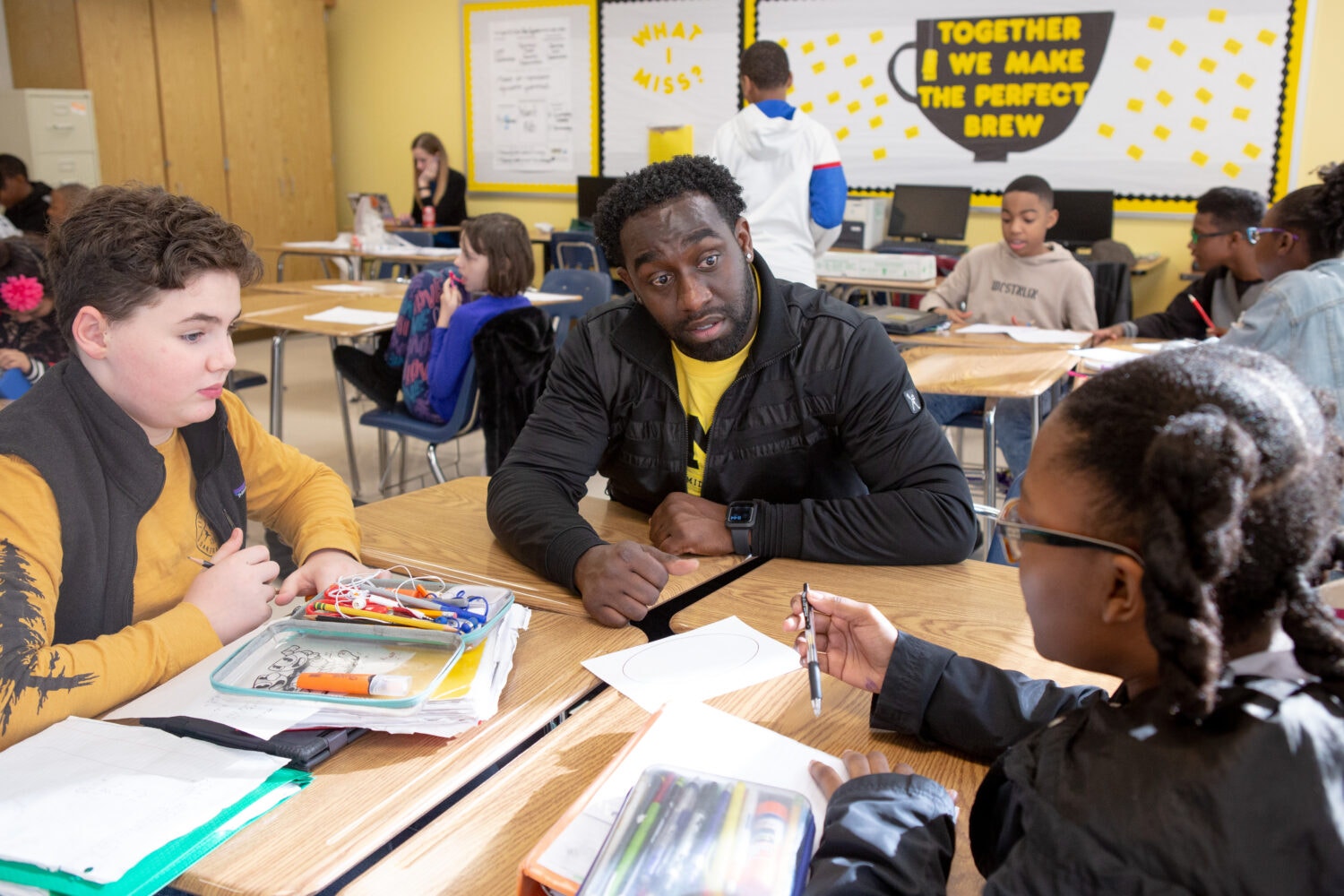 A Black teacher sits with two middle school students at lunch