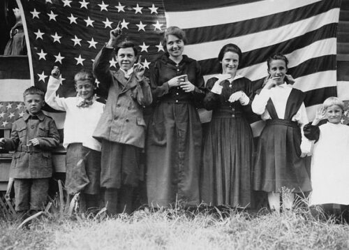 A black-and-white photo depicts children using sign language to sing the U.S. national anthem, 'The Star Spangled Banner', standing before the U.S. flag, at the St Rita School for the Deaf, in Evendale, Ohio, 1935. From left, the students are signing 'Oh, Say', 'Can You', 'See', 'By The', 'Dawn's', 'Early' and 'Light'.