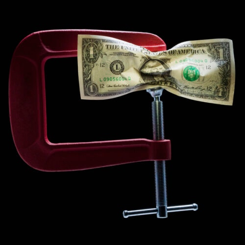 A dollar bill being squeezed in a red metal clamp